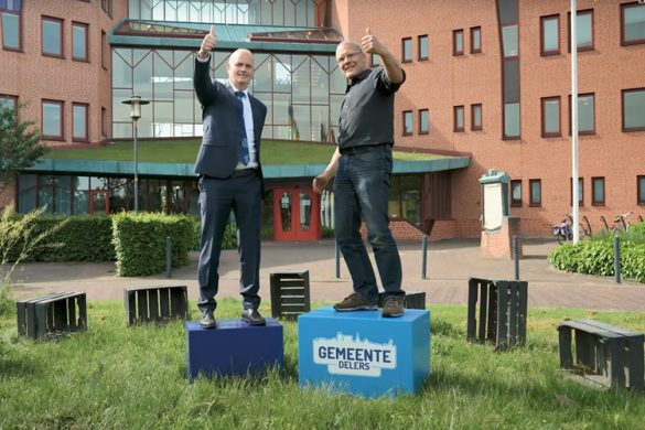 Pieter Neven, wethouder en Holger Peters, webmaster en informatieadviseur bij de Gemeente Buren staan voor het gemeentehuis op een blauw blok met logo van gemeentedelers