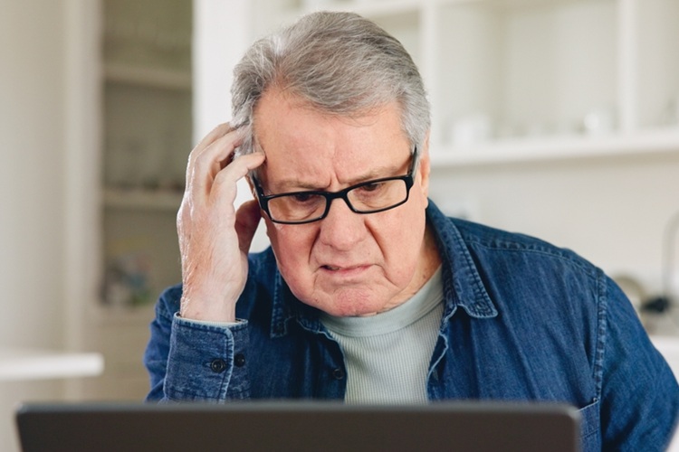 Oudere man achter laptop, moeilijk kijkend