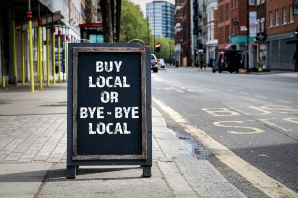 Bord met 'buy local' op het trottoir van winkelstraat