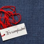 Blauwe achtergrond met rood kluwen garen. Kaartje eraan met tekst 'It's complicated'